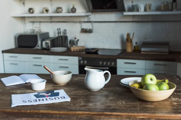 Holztisch mit Geschirr, Milchkanne, Obst, Notizbuch und Wirtschaftszeitung — Stockfoto