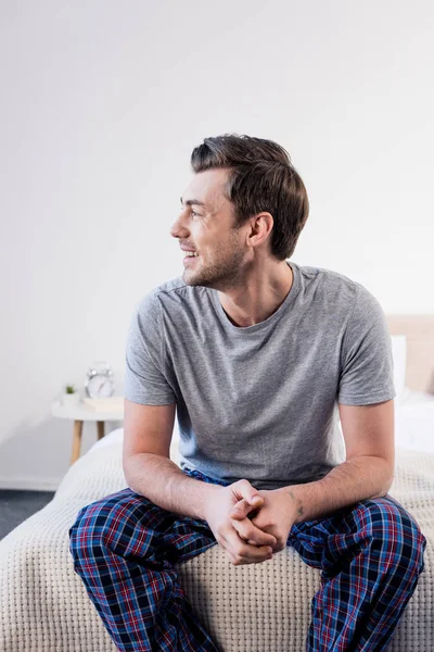 Good-looking cheerful man sitting on bedding at home and looking away — Stock Photo