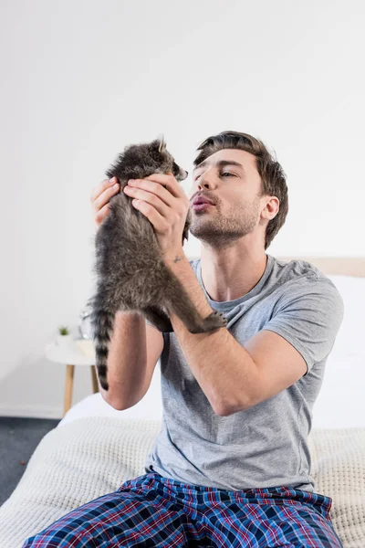 Homme heureux assis sur la literie à la maison et tenant raton laveur adorable — Photo de stock