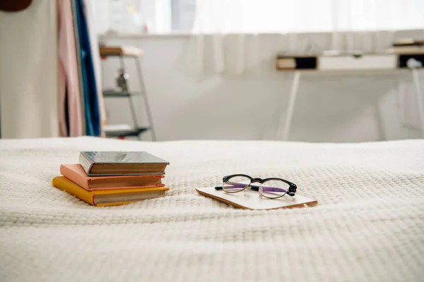 Livros e óculos na cama no quarto aconchegante claro — Fotografia de Stock