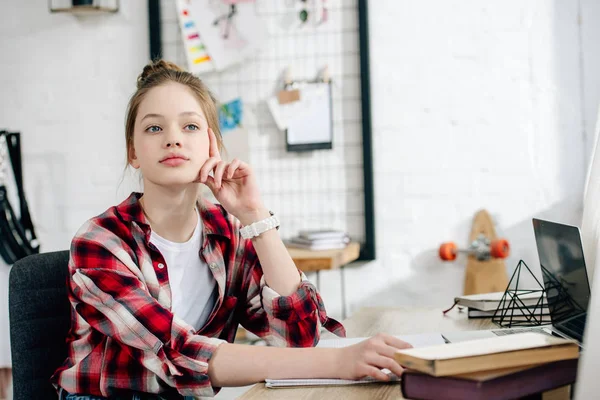 Adolescente sognante in camicia rossa a scacchi seduta a tavola con libri e distogliendo lo sguardo — Foto stock