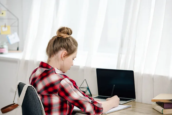 Teenager in checkered shirt writing in notebook while doing homework — Stock Photo