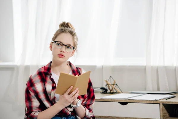 Curious teenage kid in glasses and checkered shirt reading book — Stock Photo