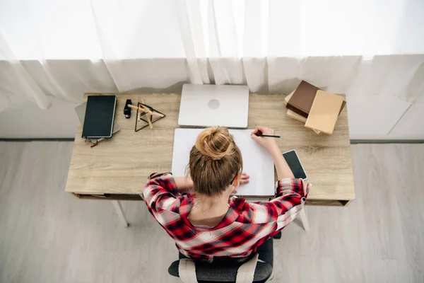 Vista aérea de adolescente con camisa a cuadros haciendo tarea en la mesa — Stock Photo