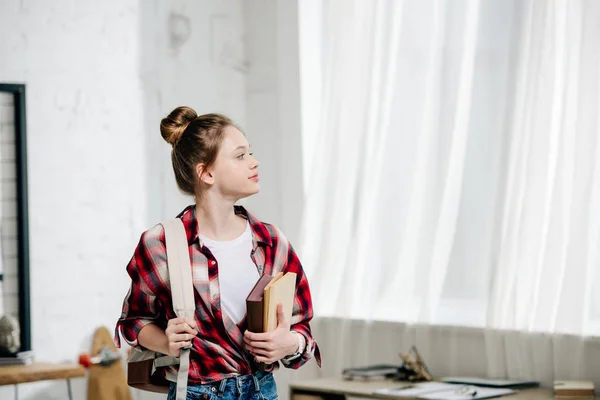 Adolescente colegiala en camisa a cuadros con mochila sosteniendo libros - foto de stock