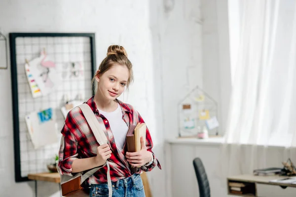 Teenage schoolgirl in checkered shirt with backpack holding books — Stock Photo