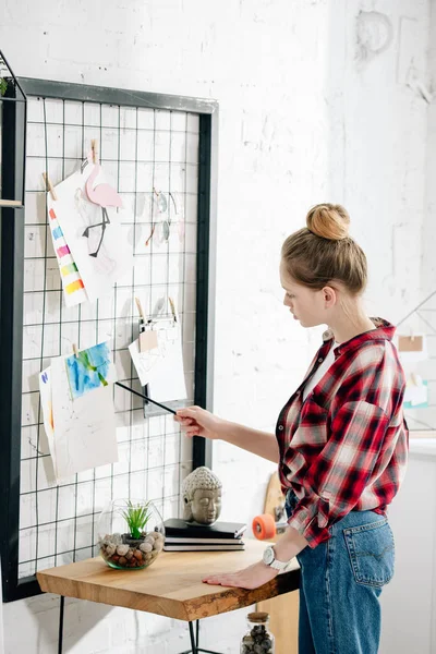 Teenager in red checkered shirt looking at pinboard in bedroom — Stock Photo