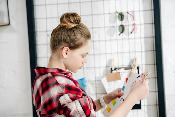 Side view of pensive teenager in checkered shirt looking at drawing — Stock Photo