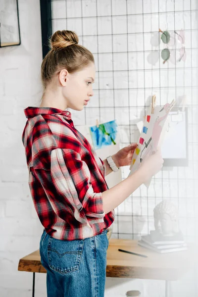 Side view of pensive teenager in checkered shirt looking at drawing — Stock Photo