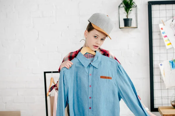 Подросток в кепке держит вешалку в синей рубашке дома — стоковое фото
