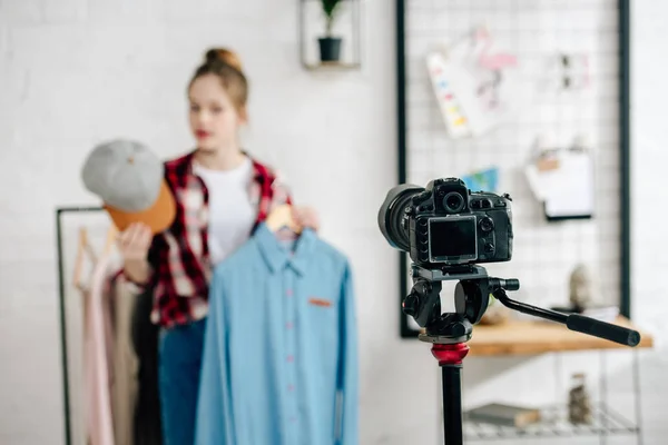 Selective focus of teenager holding cap and shirt in front of video camera — Stock Photo