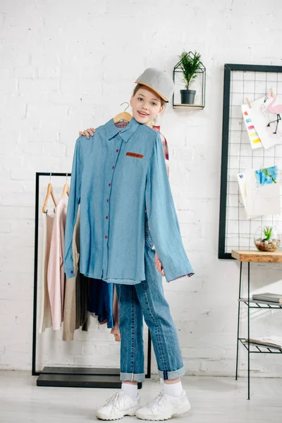 Pleine longueur vue de l'adolescent enfant en chapeau tenant cintre avec chemise bleue à la maison — Photo de stock