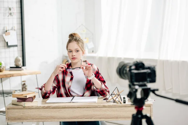 Adolescente blogueiro sentado na mesa na frente da câmera de vídeo e fazendo vídeo — Fotografia de Stock