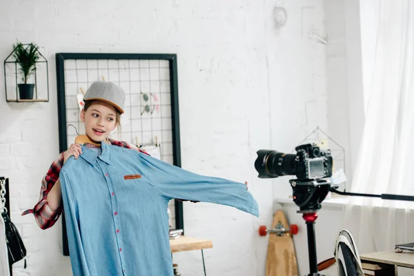 Adolescent souriant en casquette montrant chemise bleue à la caméra vidéo — Photo de stock