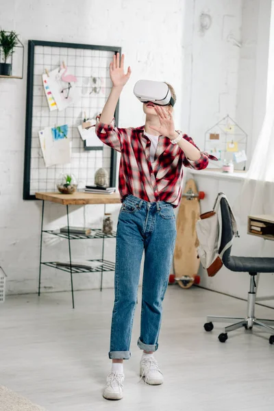 Full length view of teenager in red checkered shirt and vr headset gesturing at home — Stock Photo
