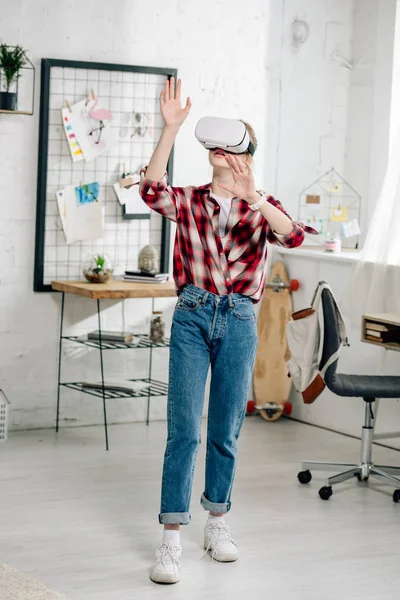 Ganzkörperansicht eines Teenagers in rot kariertem Hemd und Vr-Headset, der zu Hause gestikuliert — Stockfoto