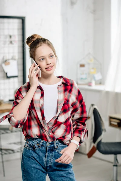 Cheerful teenager in jeans talking on smartphone at home — Stock Photo