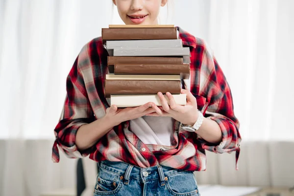 Cropped view of teenage kid in red checkered shirt holding books at home — Stock Photo