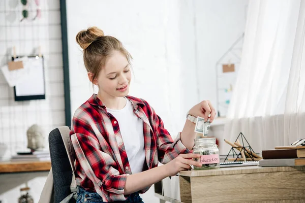 Teenager in checkered shirt putting money in the piggy bank — Stock Photo