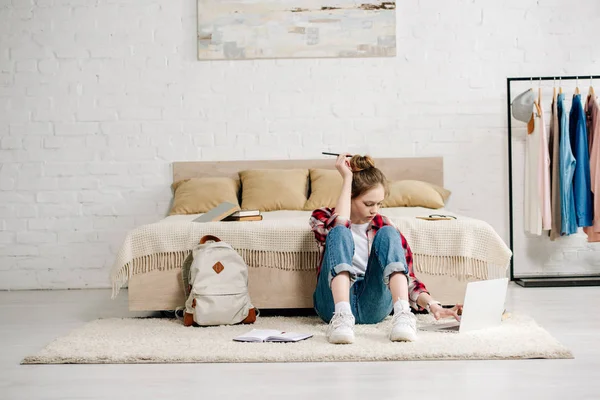 Adolescent avec ordinateur portable et livres assis sur le tapis et faire des devoirs — Photo de stock