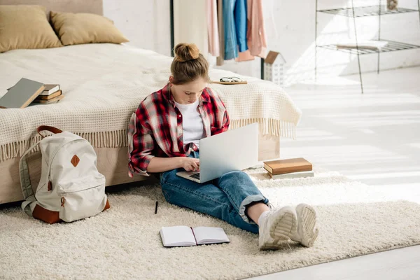 Adolescent avec ordinateur portable et livres assis sur le tapis et faire des devoirs — Photo de stock