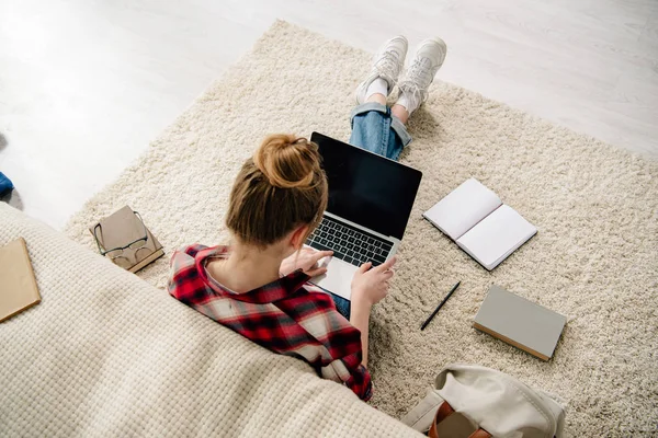 Vista aérea de adolescente con libros y portátil con pantalla en blanco haciendo la tarea - foto de stock