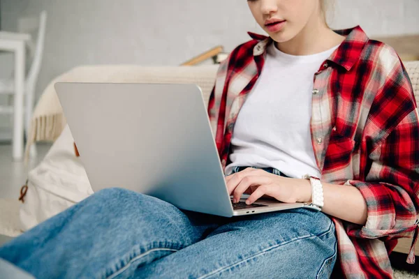 Vista recortada de un adolescente con camisa a cuadros usando un portátil - foto de stock