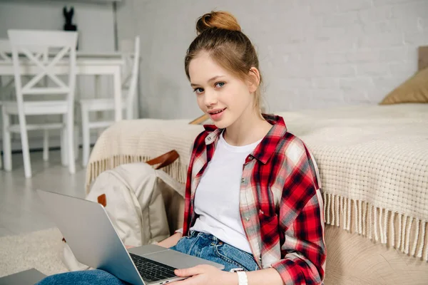 Teenage kid in checkered shirt using laptop while sitting on carpet — Stock Photo