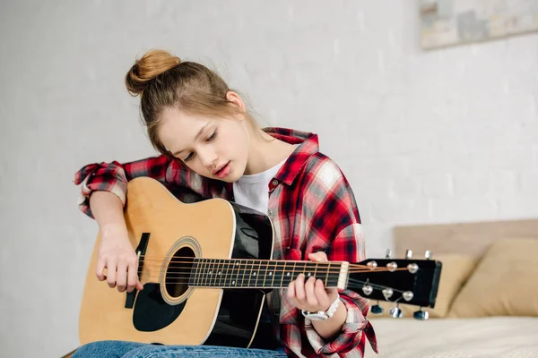 Concentrated teenager in checkered shirt playing acoustic guitar at home — Stock Photo