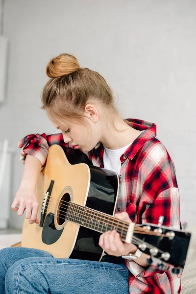 Concentrated teenager in checkered shirt playing acoustic guitar at home — Stock Photo