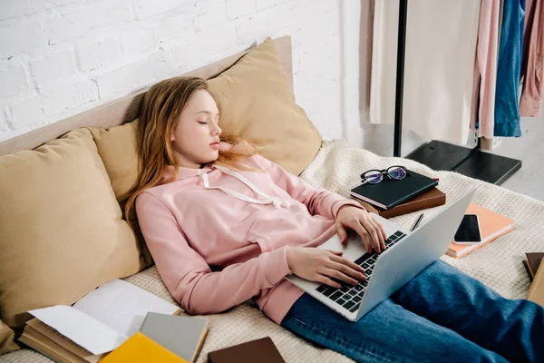 Tired teenage kid with laptop and books sleeping on bed — Stock Photo