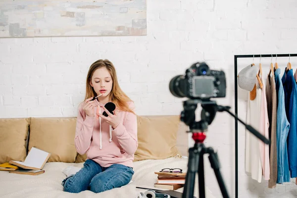 Adolescente blogueiro sentado na cama e fazendo maquiagem na frente da câmera de vídeo — Fotografia de Stock