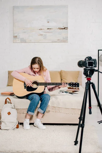 Blogger adolescente sentado en la cama y tocando la guitarra acústica frente a la cámara - foto de stock