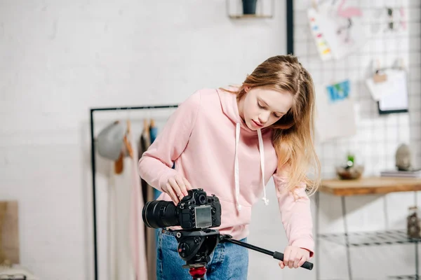 Teenage blogger in pink hoodie setting up video camera at home — Stock Photo