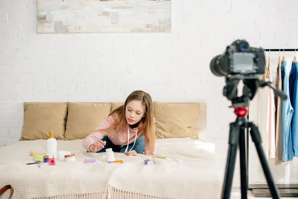 Teenage kid sitting on bed with cosmetics in front of video camera — Stock Photo