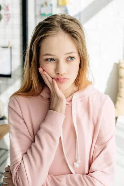 Pensive teenage kid in pink hoodie touching face and looking away — Stock Photo