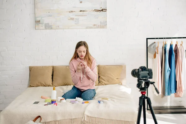 Adolescente em jeans sentado na cama com cosméticos na frente da câmera de vídeo — Fotografia de Stock