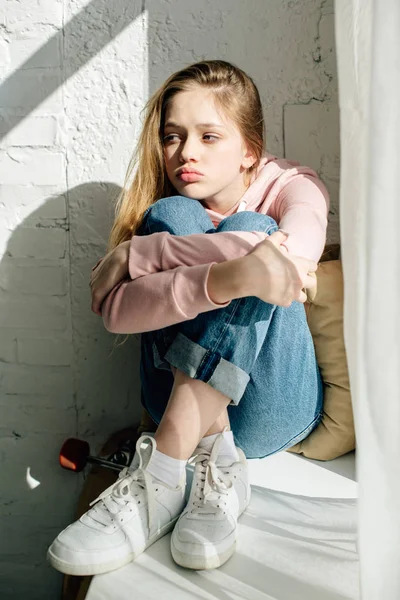 Pensive teenage kid in jeans and white sneakers sitting on window sill — Stock Photo