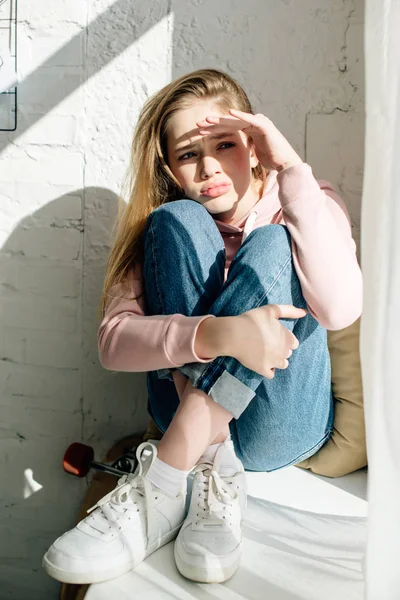 Pensive teenage kid in jeans and white sneakers sitting on window sill — Stock Photo