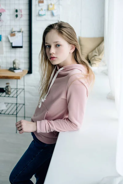 Teenage kid in pink hoodie standing near window sill — Stock Photo