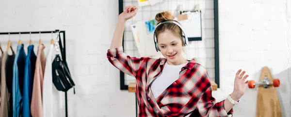 Panoramaaufnahme eines fröhlichen Teenagers im karierten Hemd, der über Kopfhörer Musik hört — Stockfoto