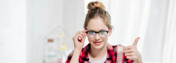 Panoramic shot of teenager in glasses showing thumb up and looking at camera — Stock Photo