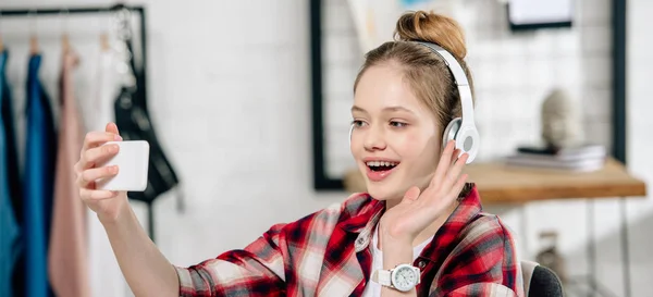 Panorama de disparo de adolescente en auriculares saludando de la mano durante la videollamada - foto de stock