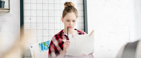 Foto panorámica de adolescente concentrado sosteniendo lápiz y papeles - foto de stock