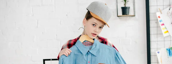 Панорамний знімок підлітка в шапці, що тримає вішалку з синьою сорочкою — стокове фото