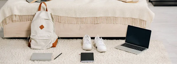 Foto panoramica di sneakers bianche, laptop con schermo bianco e zaino su moquette — Foto stock