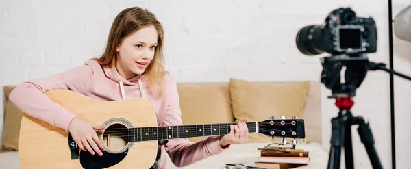 Foto panorámica del bloguero adolescente tocando la guitarra acústica frente a la cámara de video - foto de stock