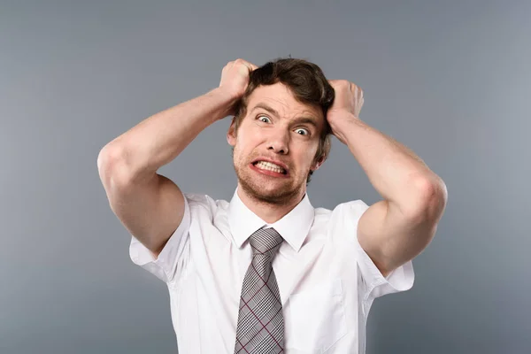 Divertido empresario estresado cogido de la mano en la cabeza sobre fondo gris — Stock Photo