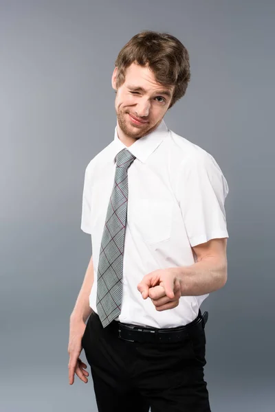 Schlitzohriger Geschäftsmann zeigt mit dem Finger auf Kamera und zwinkert auf grauem Hintergrund — Stockfoto