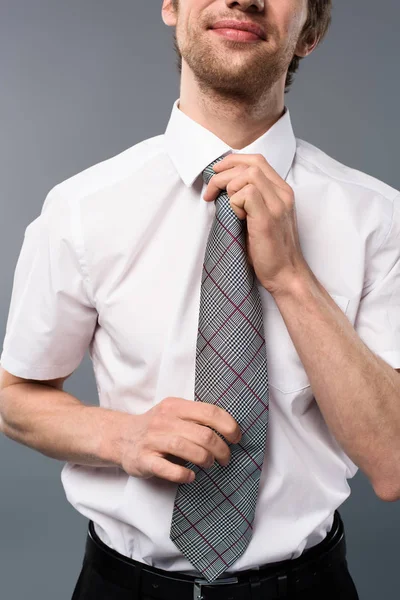 Cropped view of cheerful businessman tying tie on grey background — Stock Photo